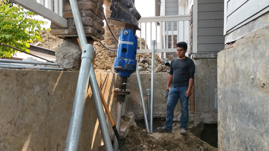 Fort August Construction installing a helical pier beneath a front porch to stabilize a residential foundation