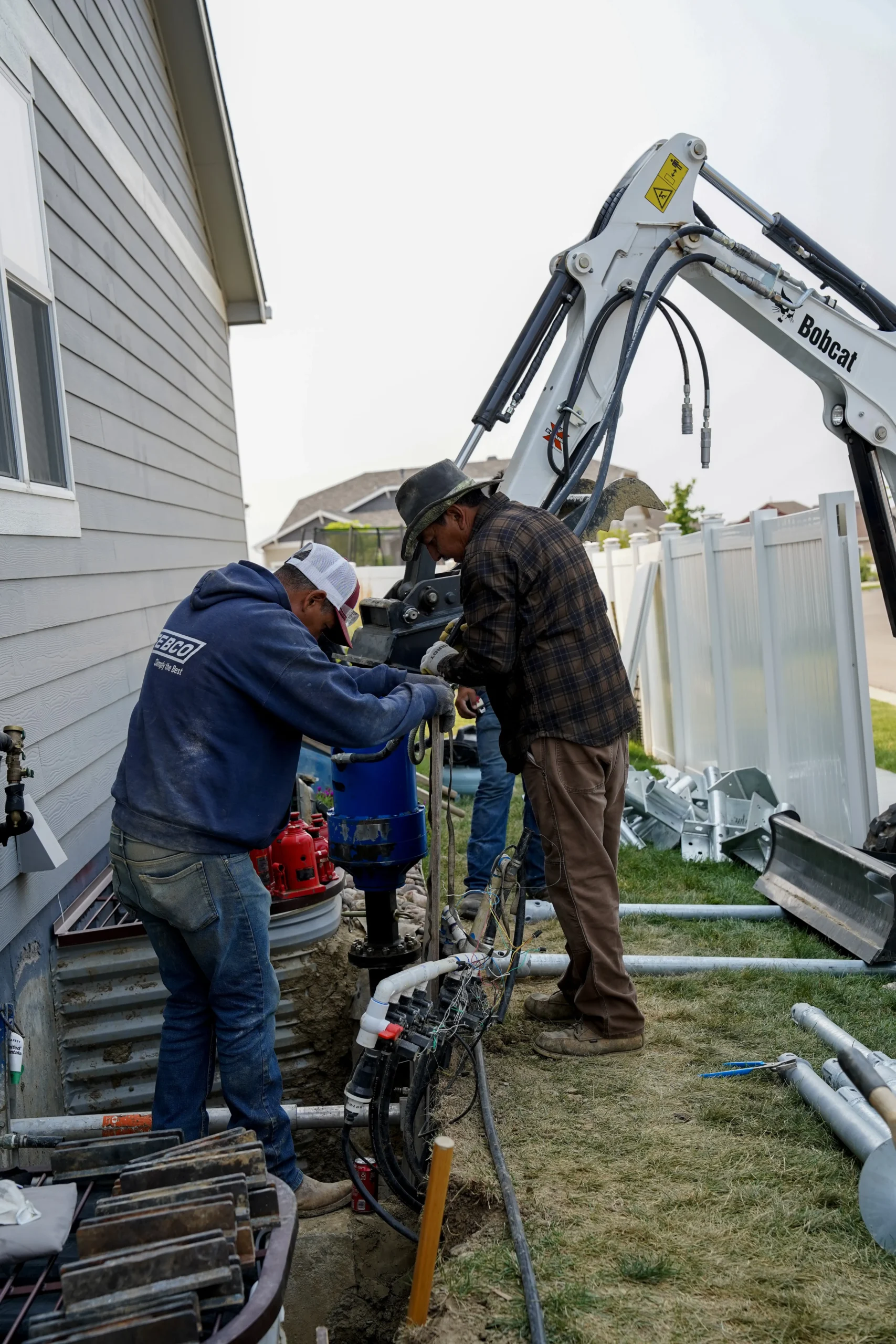 Fort August Construction crew installing a helical pier along the side of a residential home for foundation repair