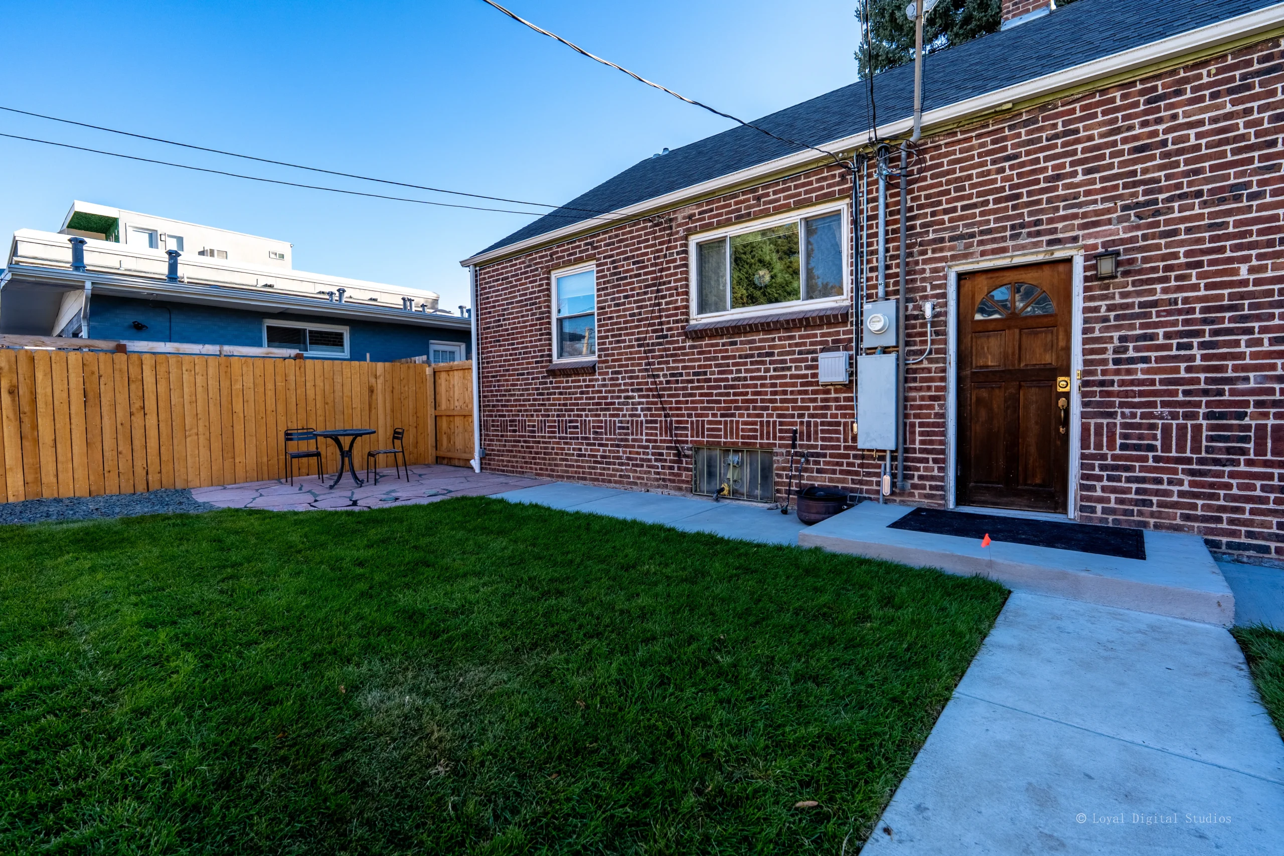 Fort August Construction completed backyard concrete walkway and patio installation beside a brick home in Denver, Colorado.